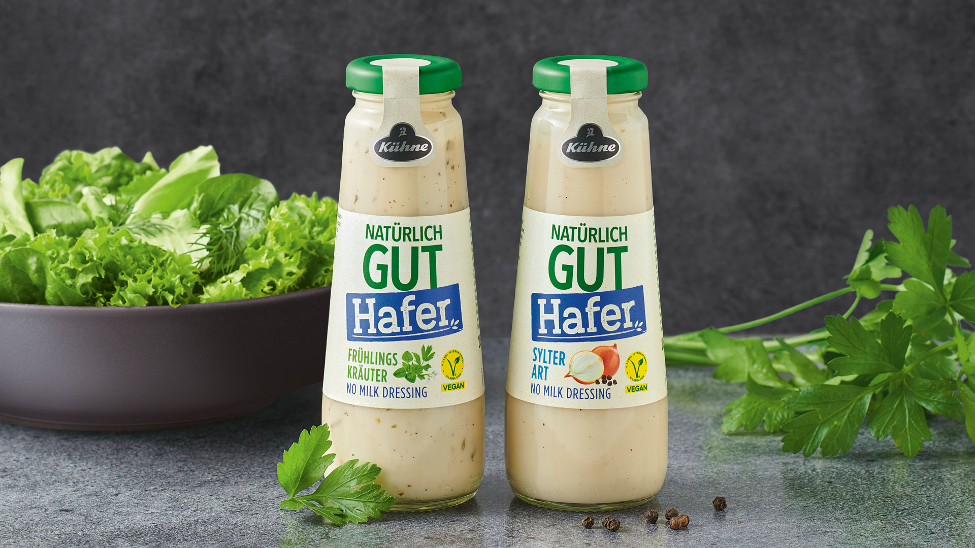 Zwei Kühne Natürlich Gut Hafer Dressings vor einer Salatschale und Kräutern