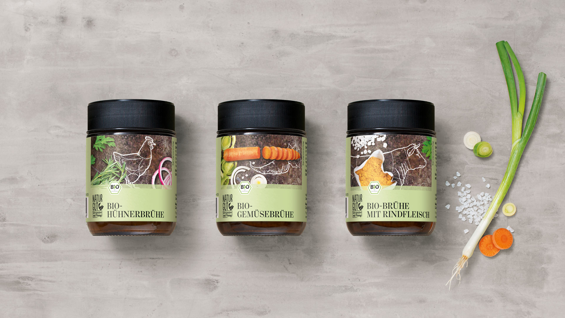Penny Naturgut Bio Hühnerbrühe, Bio Gemüsebrühe und Bio Brühe mit Rindfleisch Verpackungsdesigns mit Zutaten auf grauem Beton Untergrund