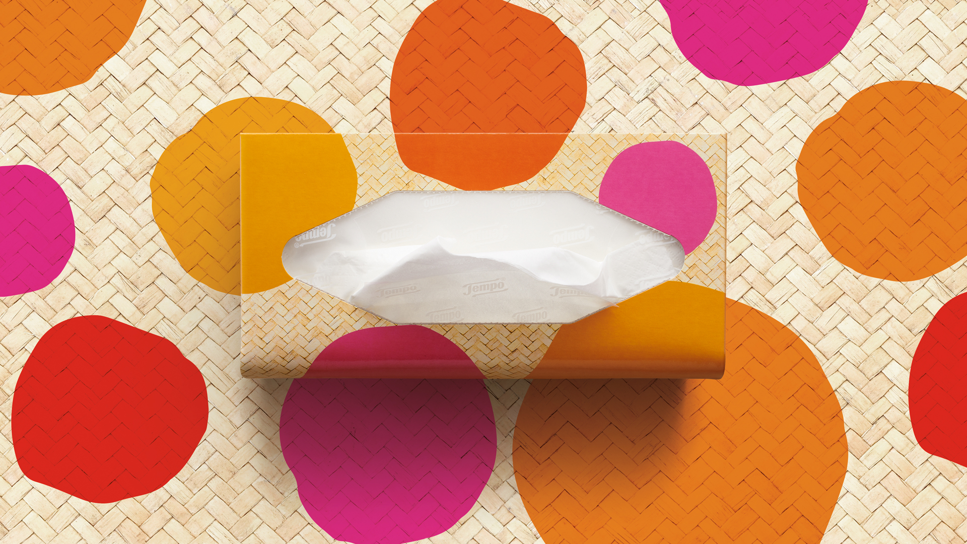 Tempo Taschentuchbox im sommerlichen Bastdesign mit bunten, handgemalten Farbklecksen in Pink, Orange, Rot und Gelb – vor einem farblich abgestimmten Hintergrund, der das Muster der Verpackung spielerisch weiterführt.
