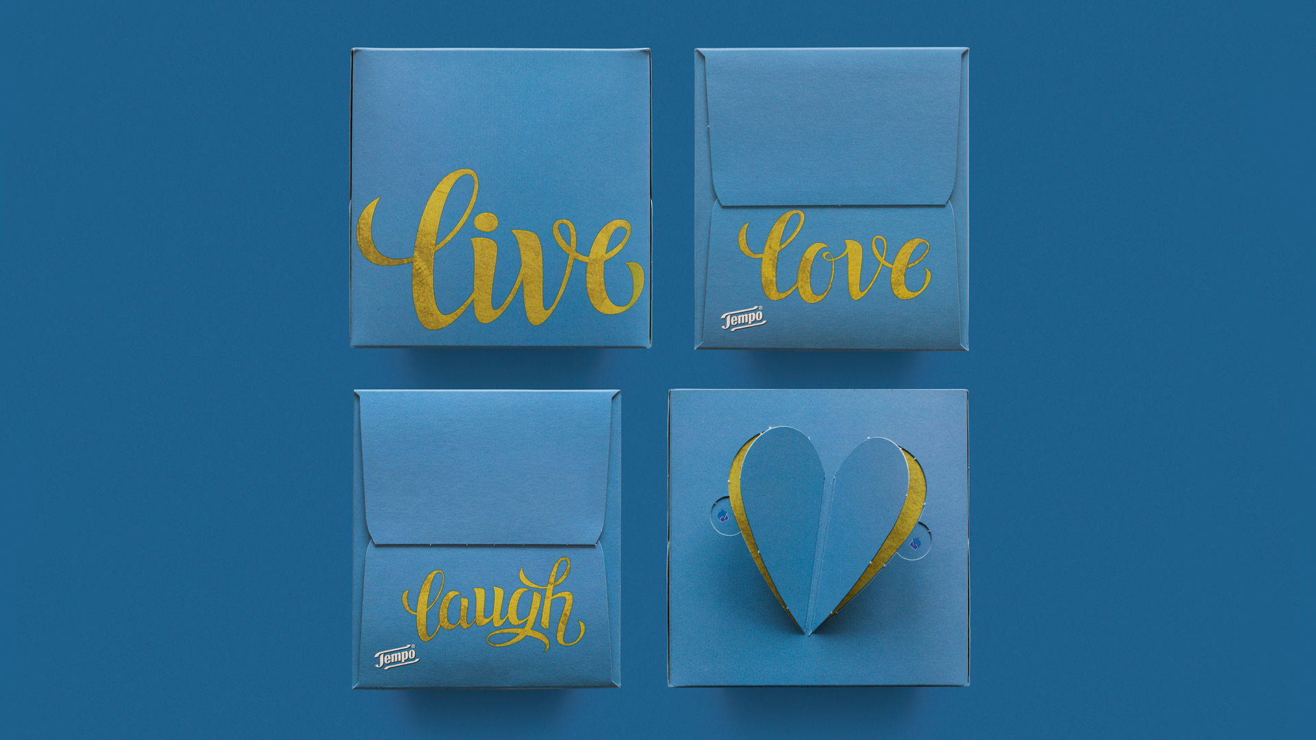 Vier Tempo Taschentuchboxen in elegantem Blau mit goldglänzender Typografie – versehen mit den inspirierenden Worten „live“, „love“, „laugh“ sowie einer herzförmigen Stanzung