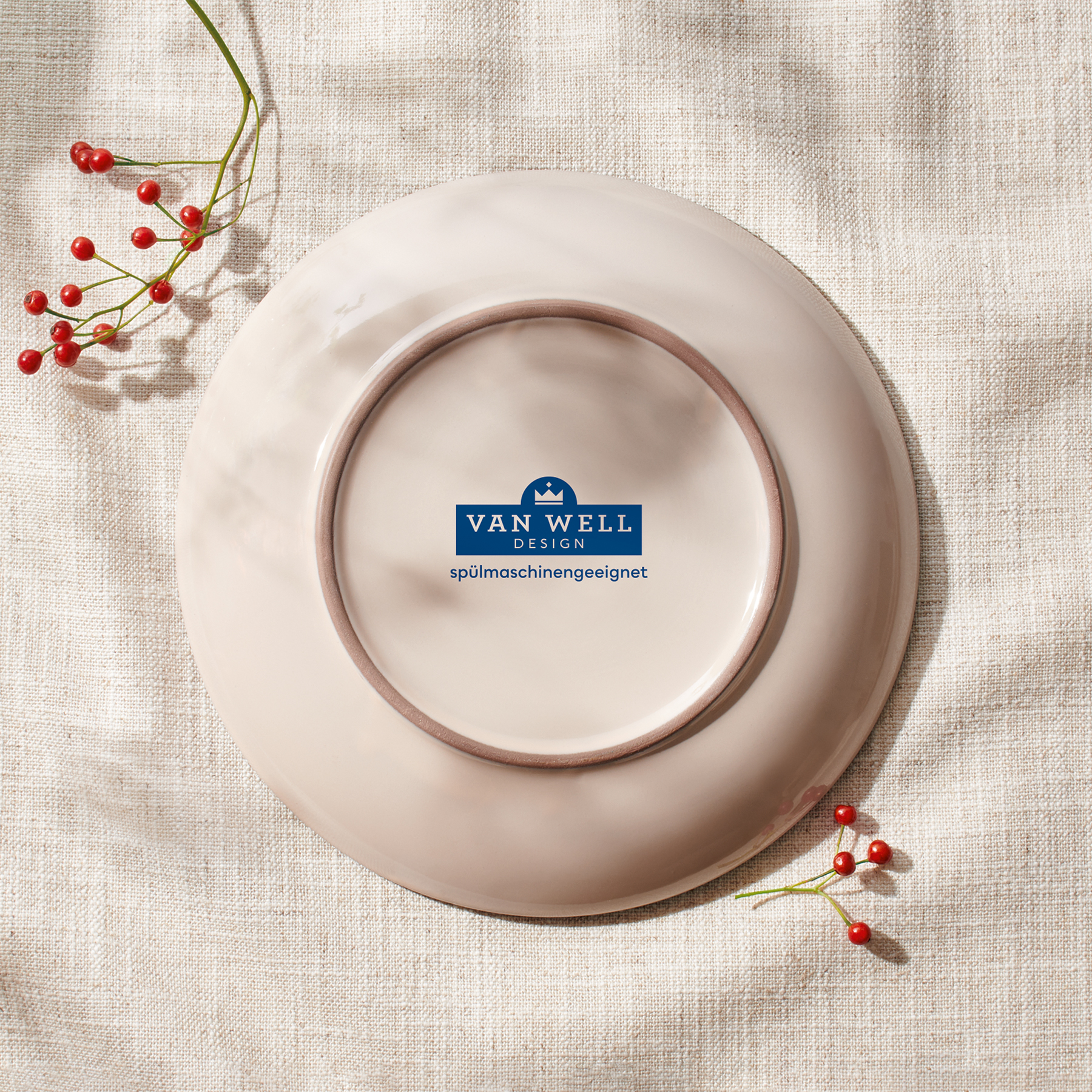 Rückseite eines Tellers aus der Van Well Design Serie ‚ROYAL‘ auf Leinentuch mit roten Zierbeeren – zentrales Markenlogo und Hinweis ‚spülmaschinengeeignet‘ dezent im Fokus, in harmonischer Lichtstimmung inszeniert.