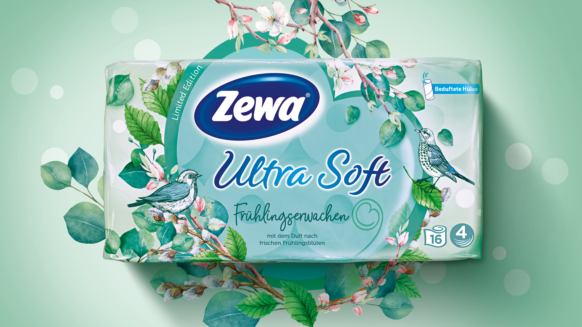 Frühlingshafte Limited Edition von Zewa Ultra Soft: Toilettenpapierverpackung mit floraler Illustration, zarten Blüten, Singvögeln und dem Schriftzug ‚Frühlingserwachen – mit dem Duft nach frischen Frühlingsblüten‘ auf mintgrünem Hintergrund mit sanftem Lichtspiel.
